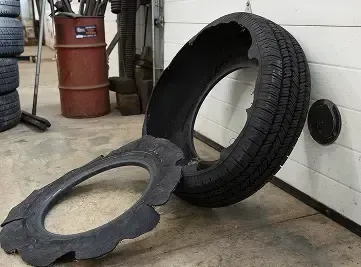 Damaged tire in a garage, with a large piece torn away, rim exposed.