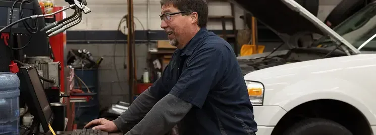 Mechanic working on a car in a garage, using a computer.