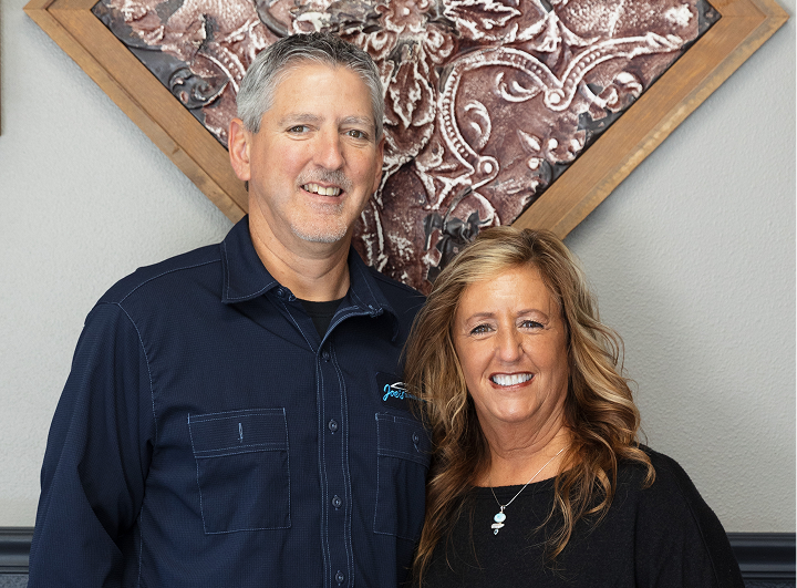 Man and woman smiling, posed in front of decorative wall art. They are indoors. | Joe's Slinger Service