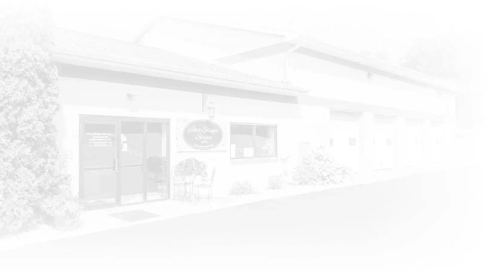 Faded white exterior of a building with a door, windows, and bushes.