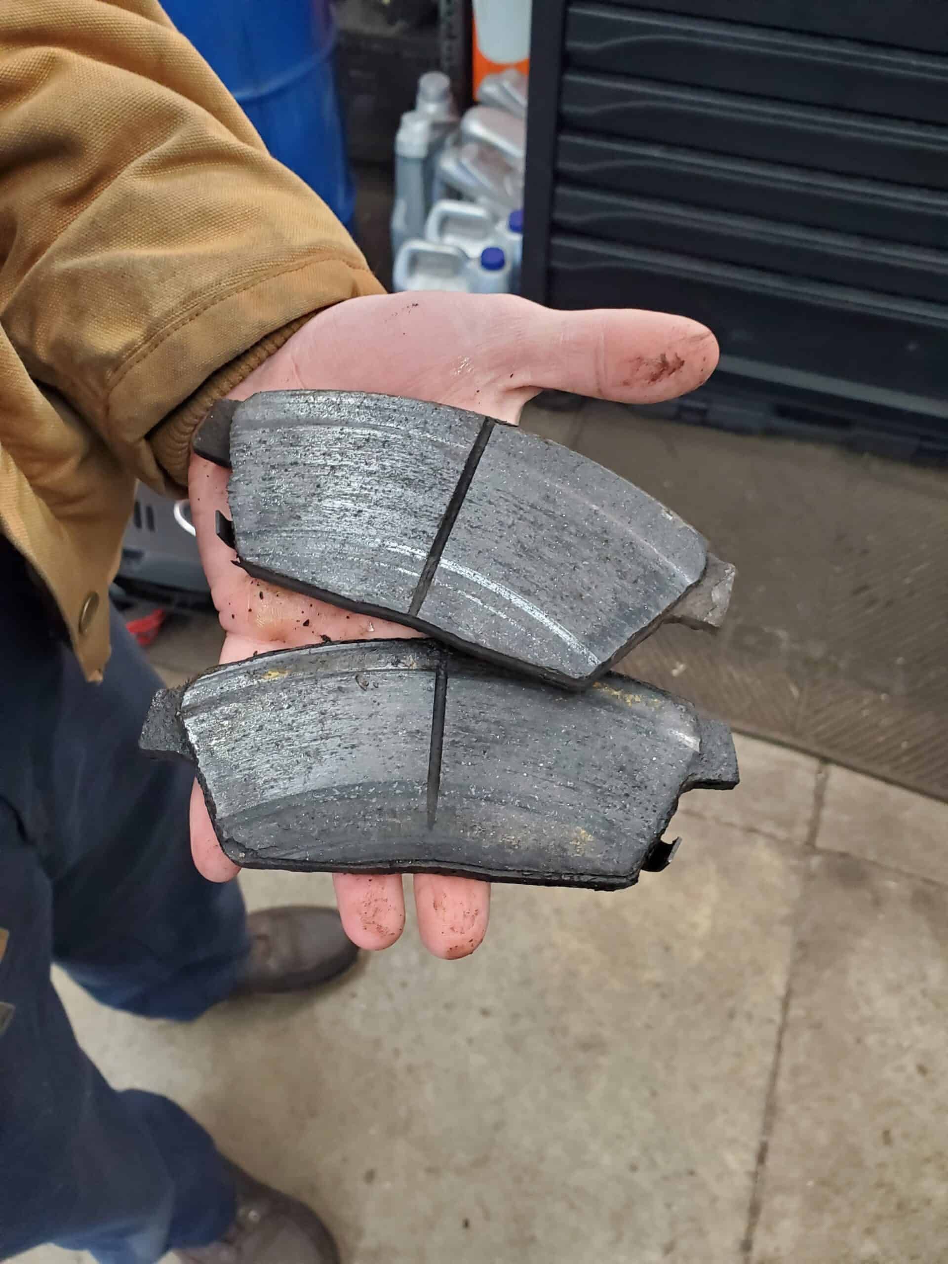 A hand holding two worn brake pads. | Joe's Slinger Service