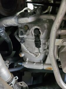 Car air conditioning compressor in an engine bay, with connected wires and tubes. | Joe's Slinger Service