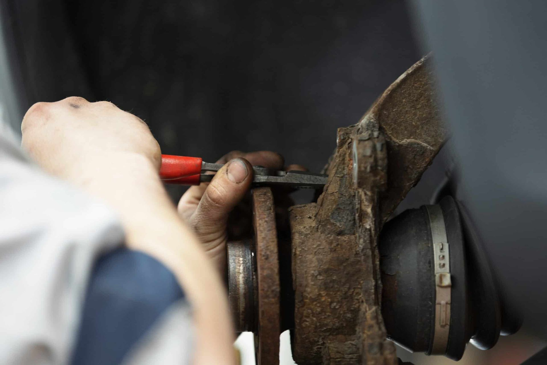 Mechanic using pliers on a rusty car part, possibly a wheel hub assembly. | Joe's Slinger Service