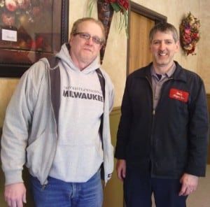 Two men stand indoors; one in a grey Milwaukee hoodie and jeans, the other in a navy jacket and work shirt, both smiling. | Joe's Slinger Service