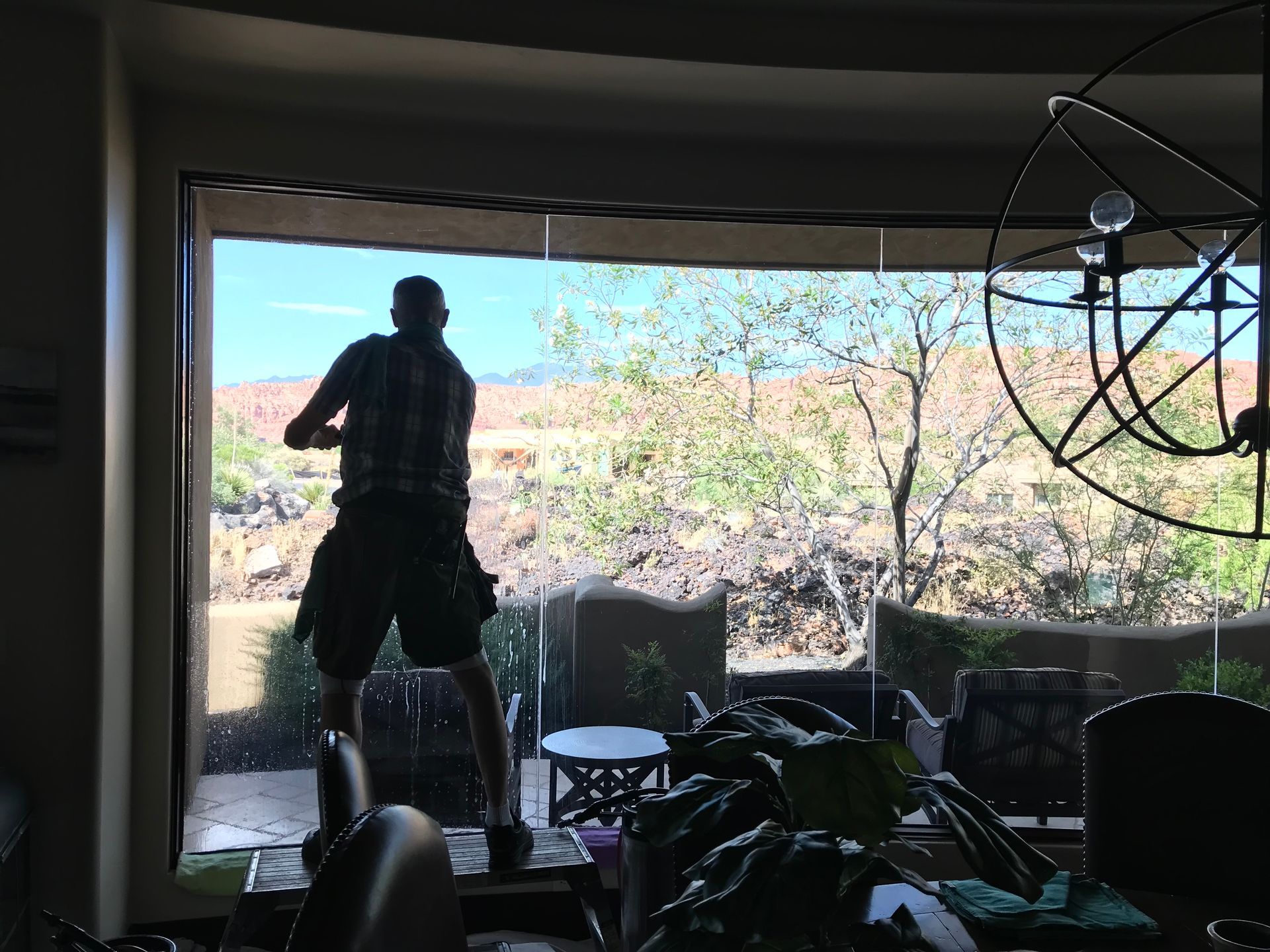 A man is cleaning a large window in a living room.