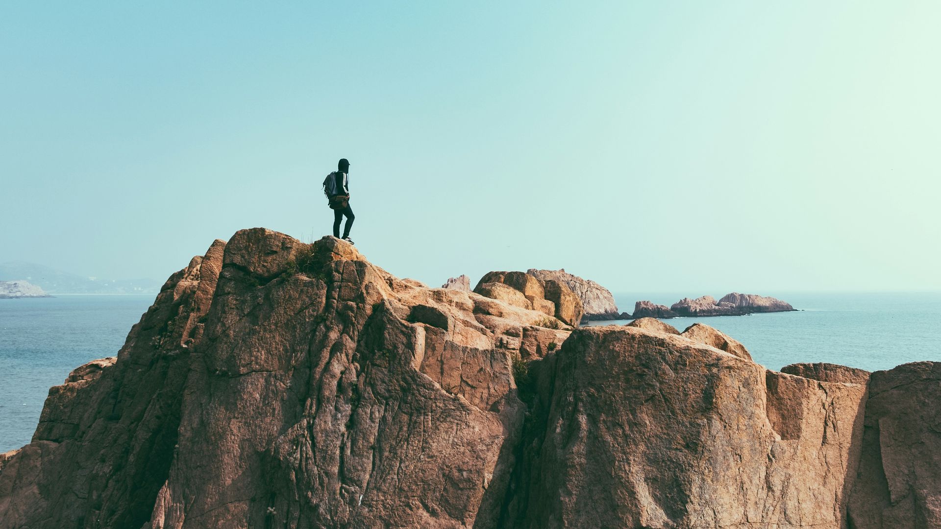 A man is standing on top of a rocky mountain overlooking the ocean.