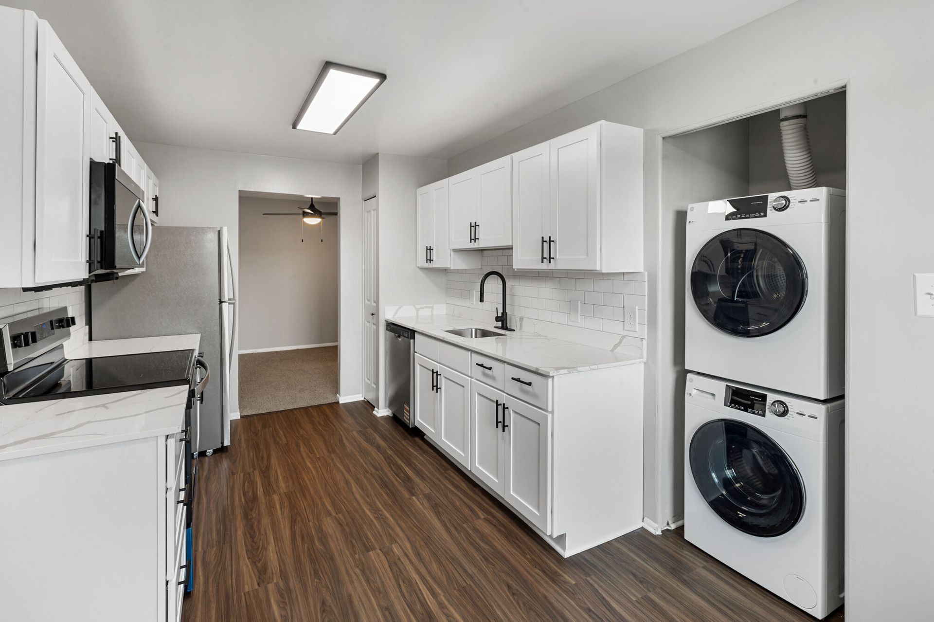 Bright kitchen with white cabinets, stainless-steel appliances, and a stacked washer/dryer in a closet.