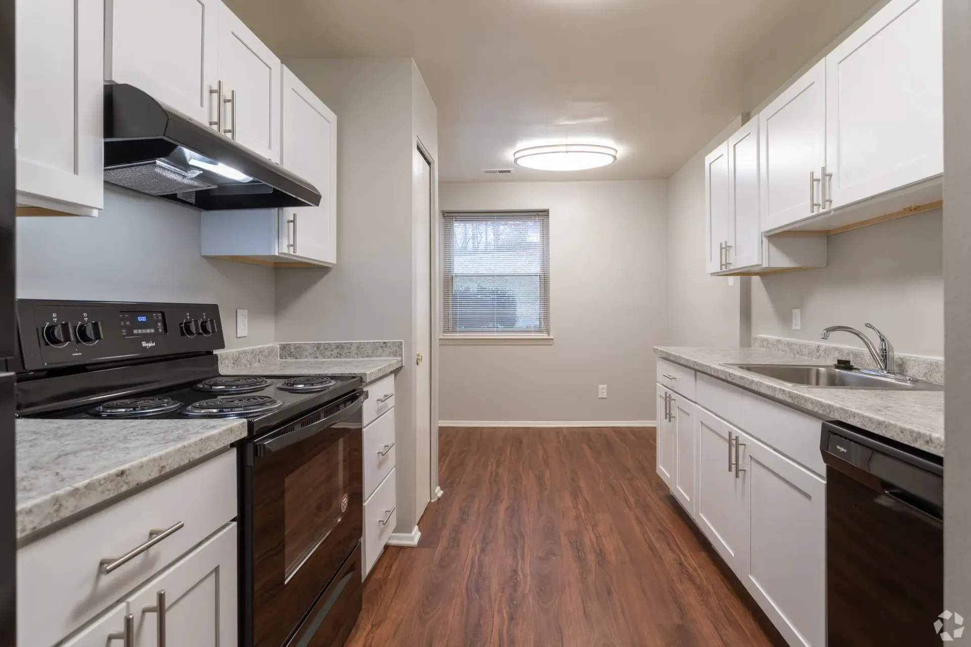 Bright galley kitchen with white cabinets, a stainless steel stove and sink, and wood-look flooring.