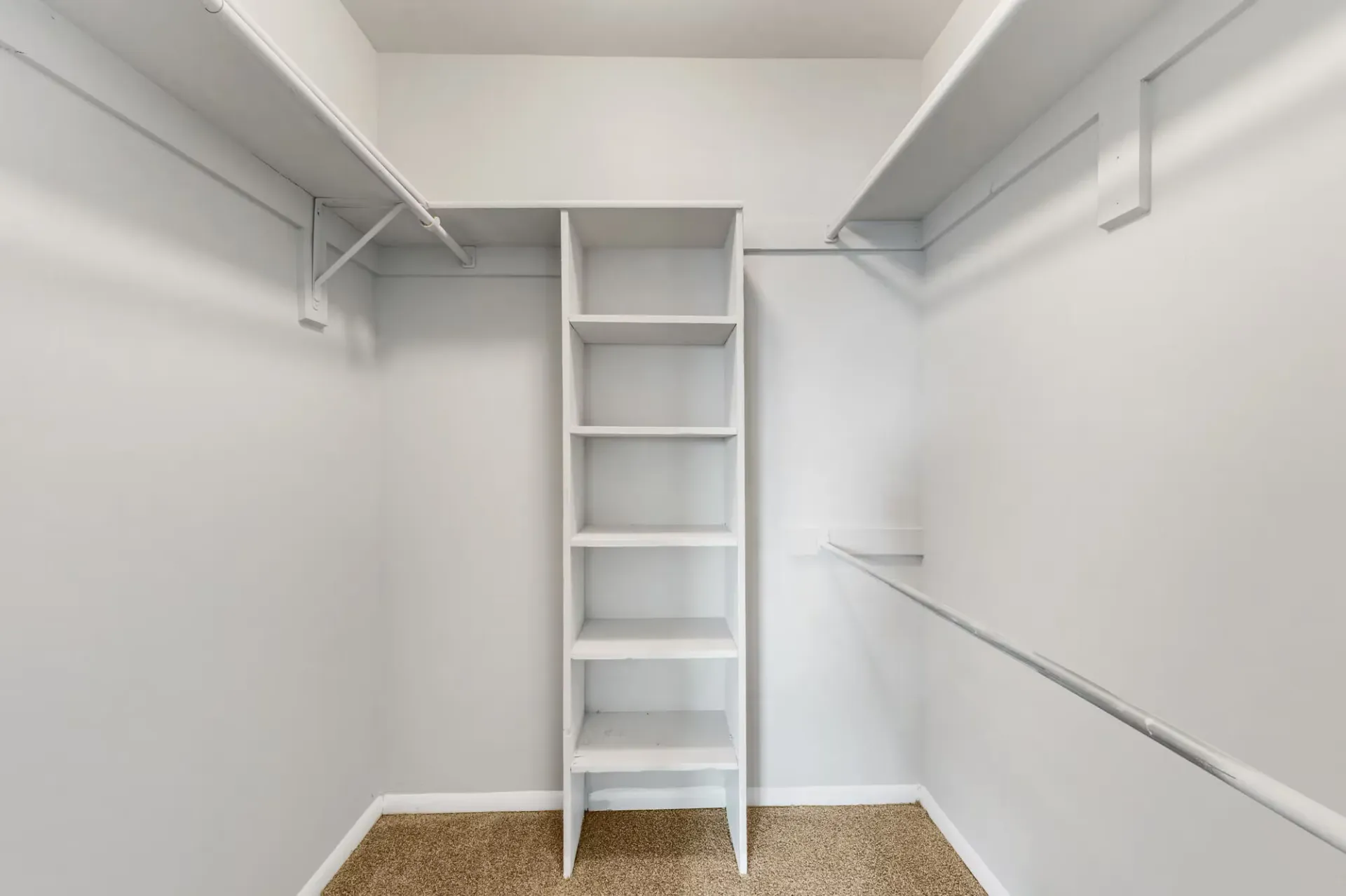 Interior of a walk-in closet with white shelving and hanging rods.