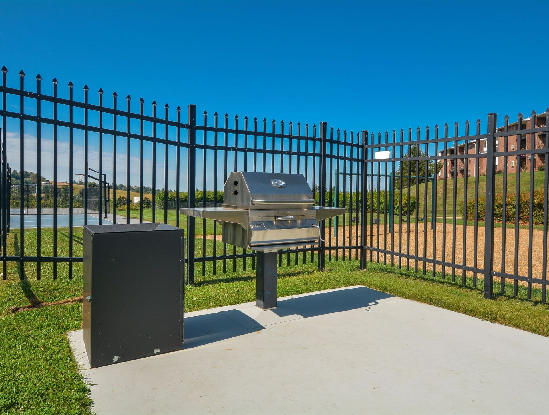 Outdoor stainless steel BBQ grill on a concrete pad with a storage cabinet, fenced yard.