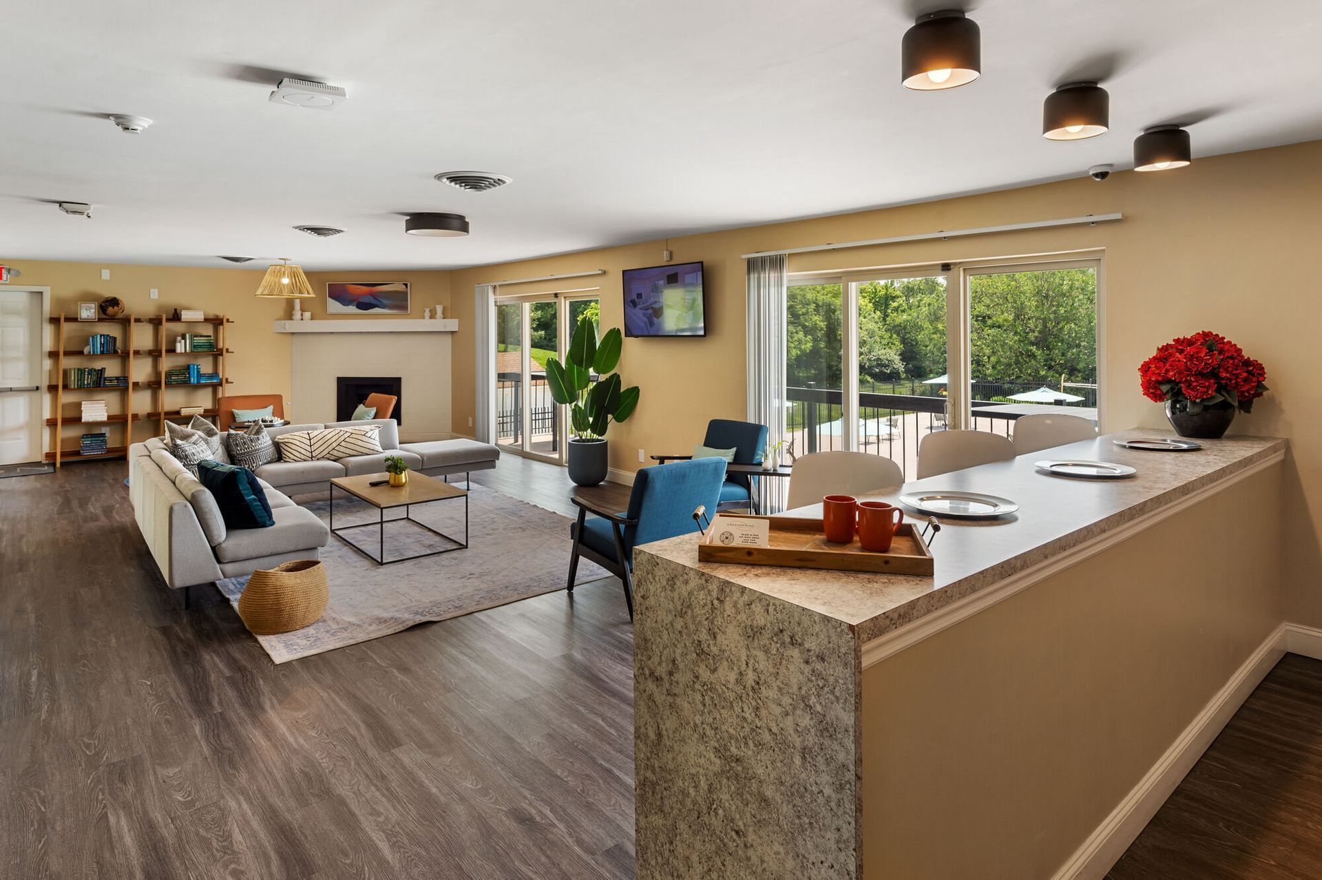 Indoor community lounge with sofa, chairs, a fireplace, TV, bookshelf, and a bar-height counter.
