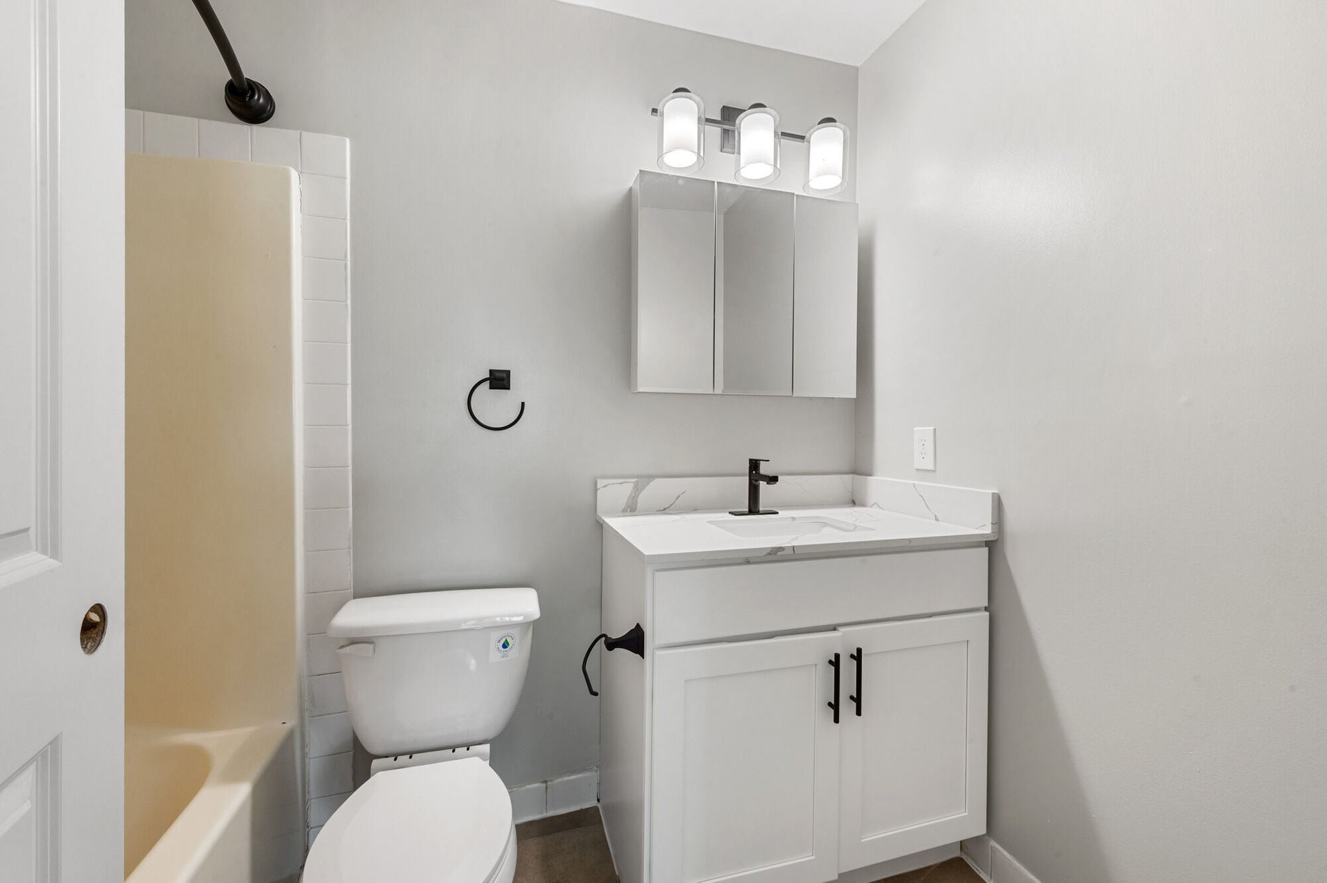 Small contemporary bathroom with white vanity, black faucet, mirror cabinet, black towel ring, and a tub/shower.