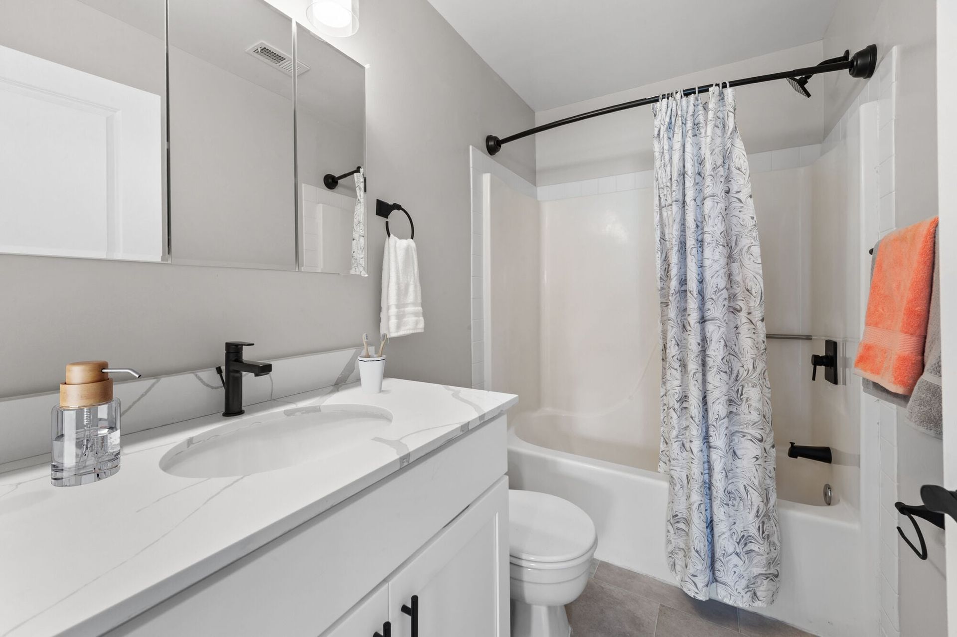 Bathroom with white vanity, black faucet, mirrored cabinets, toilet, and tub with curved shower rod.