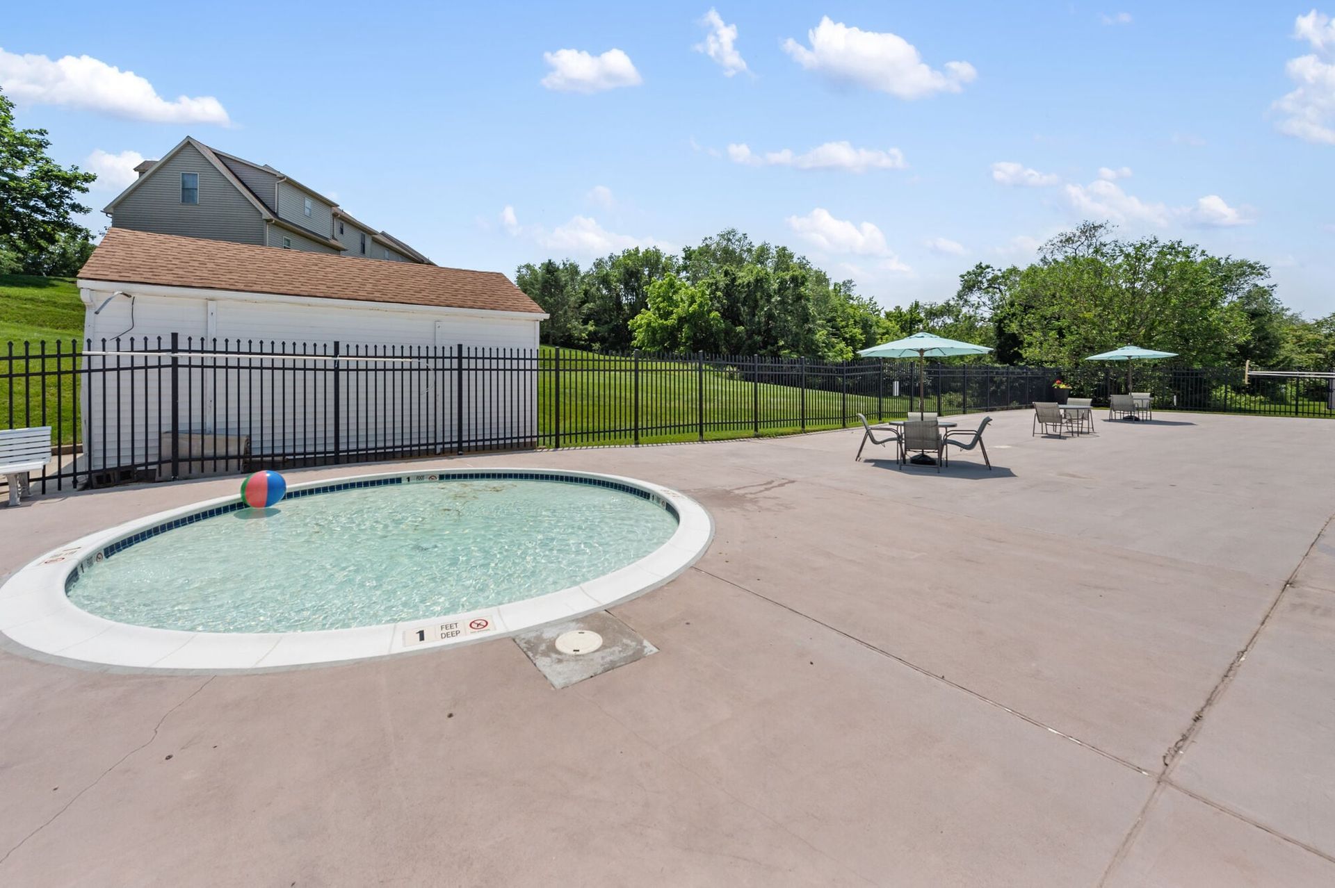 Outdoor pool area with a circular pool, black metal fence, and seating under umbrellas.