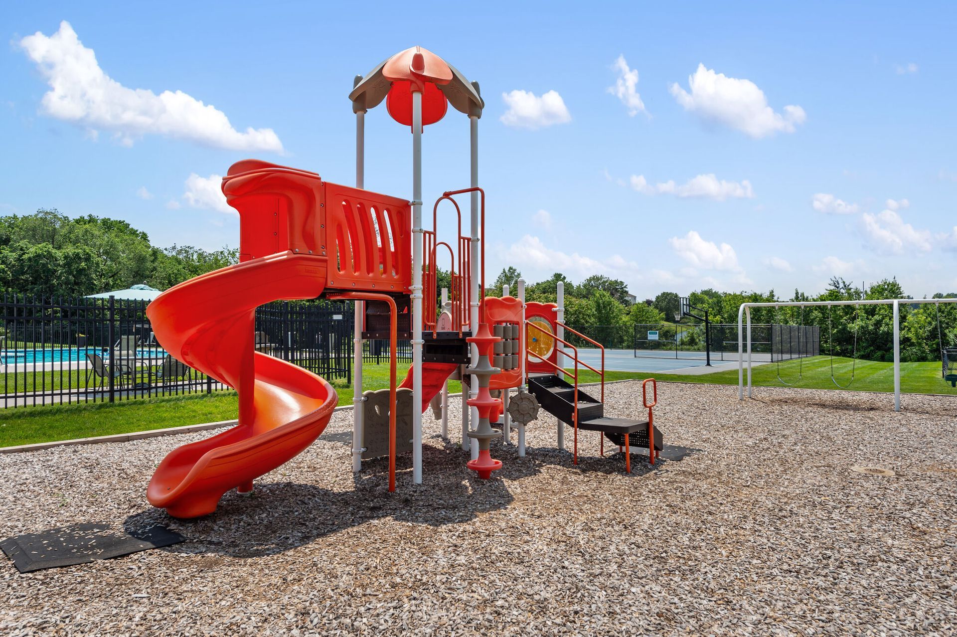 Orange playground slide at a community amenity area with a pool and sports court visible in the background.
