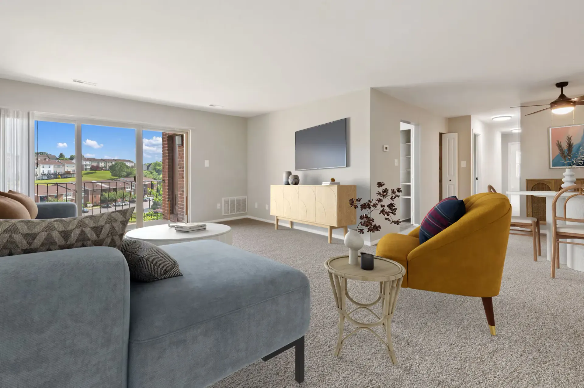 Living room in a modern apartment with a blue sofa, mustard chair, coffee table, TV on the wall, and a sliding balcony door.