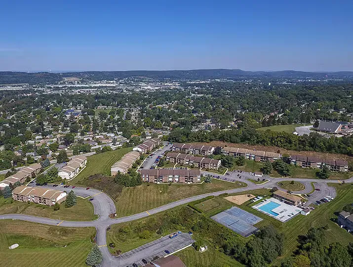 Aerial view of a multifamily community with buildings, roads, green spaces, and a swimming pool.