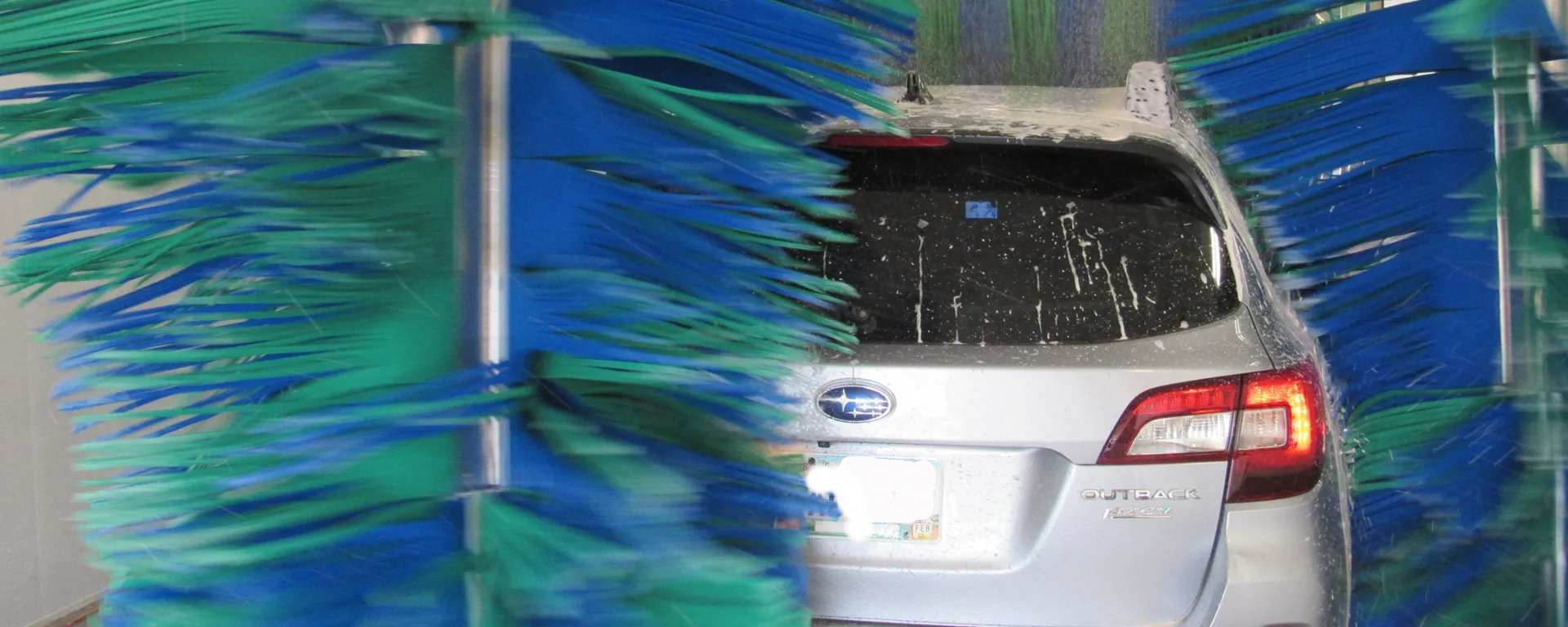 A car is going through a car wash with blue and green brushes.