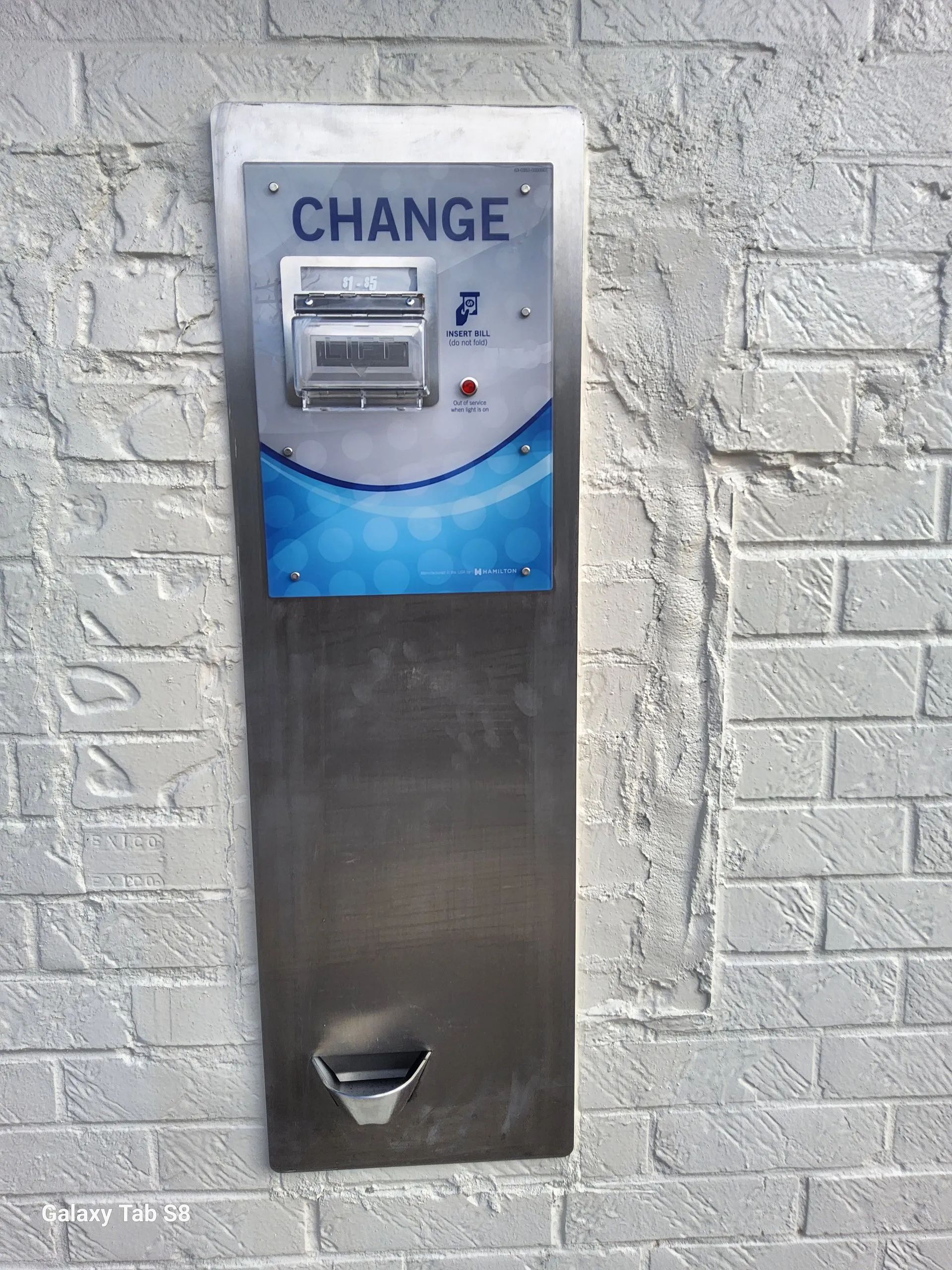 A change machine is mounted on a brick wall