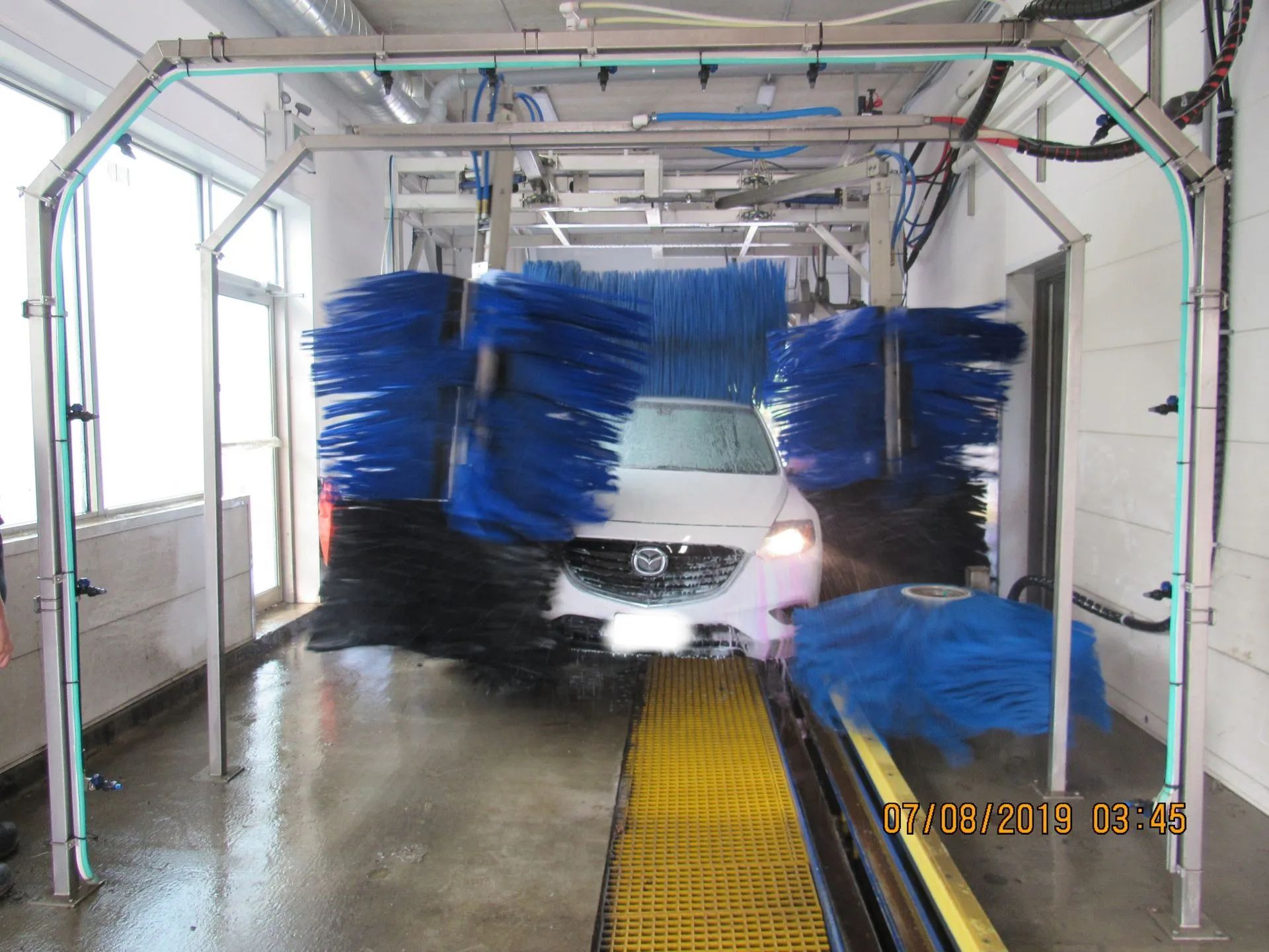 A white car is going through a car wash with blue brushes.