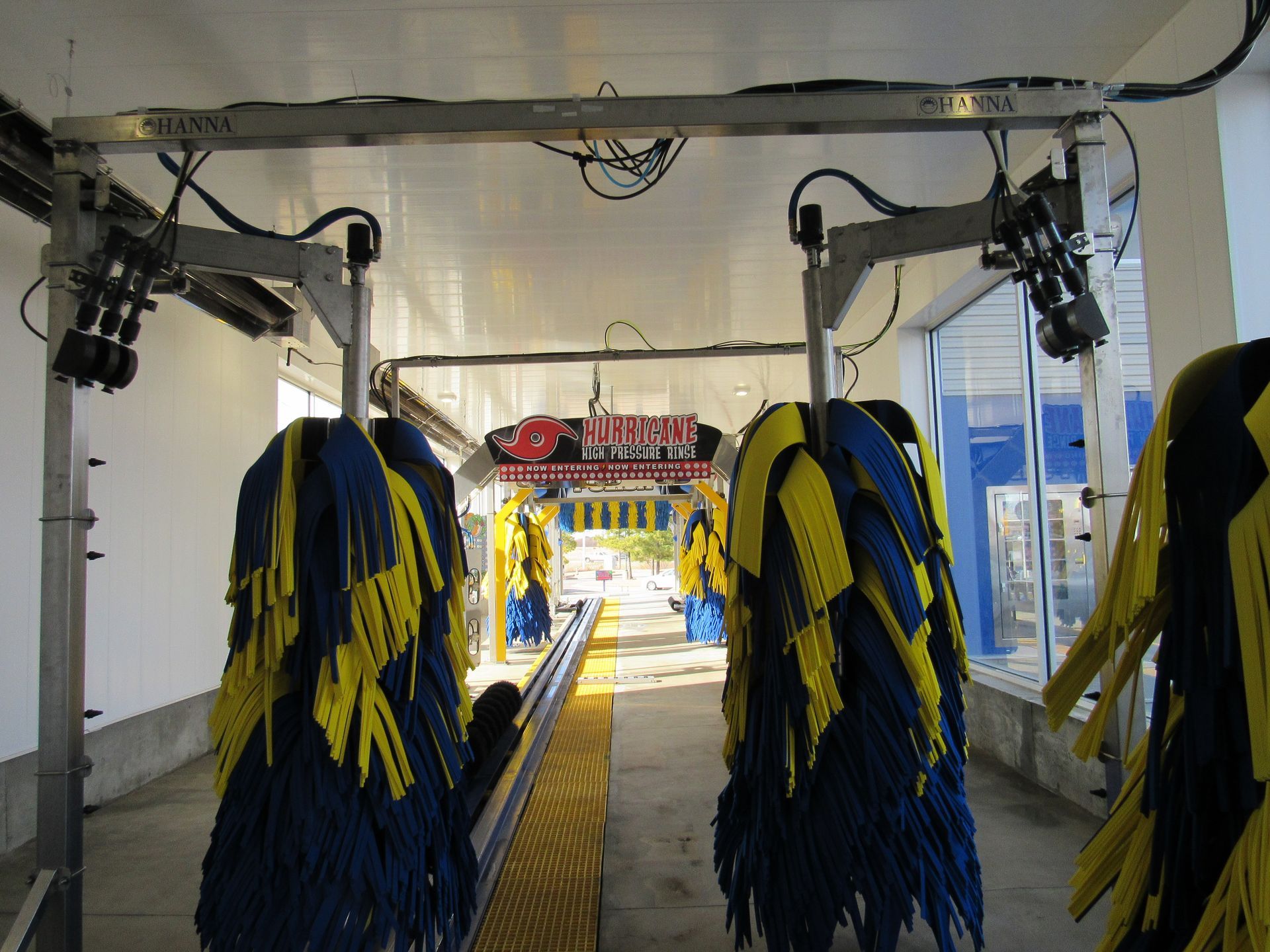 Inside a car wash, view from the entrance. Blue and yellow brushes hang down, ready to clean cars.