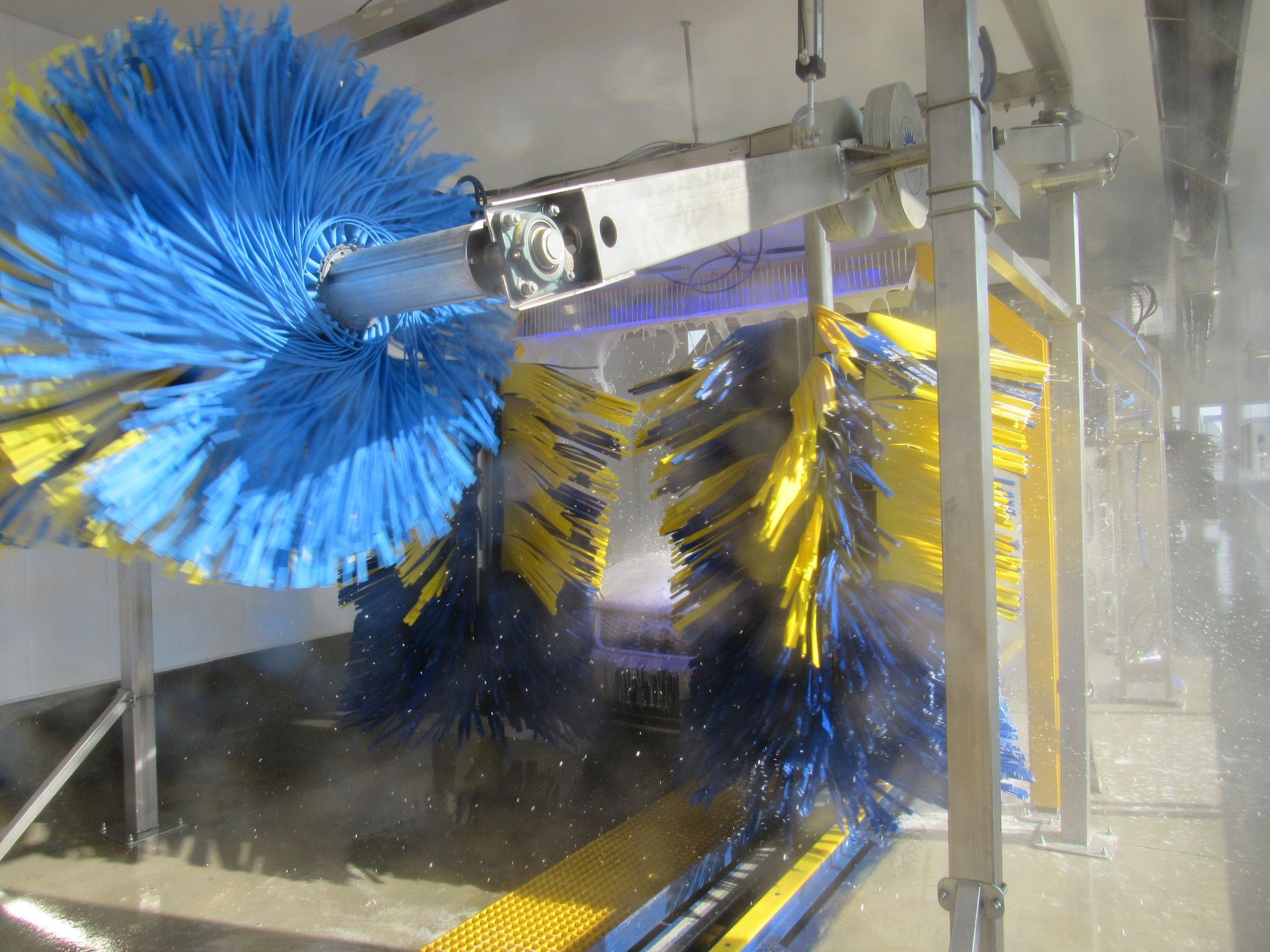 Car wash with blue and yellow brushes spraying water inside a bay.