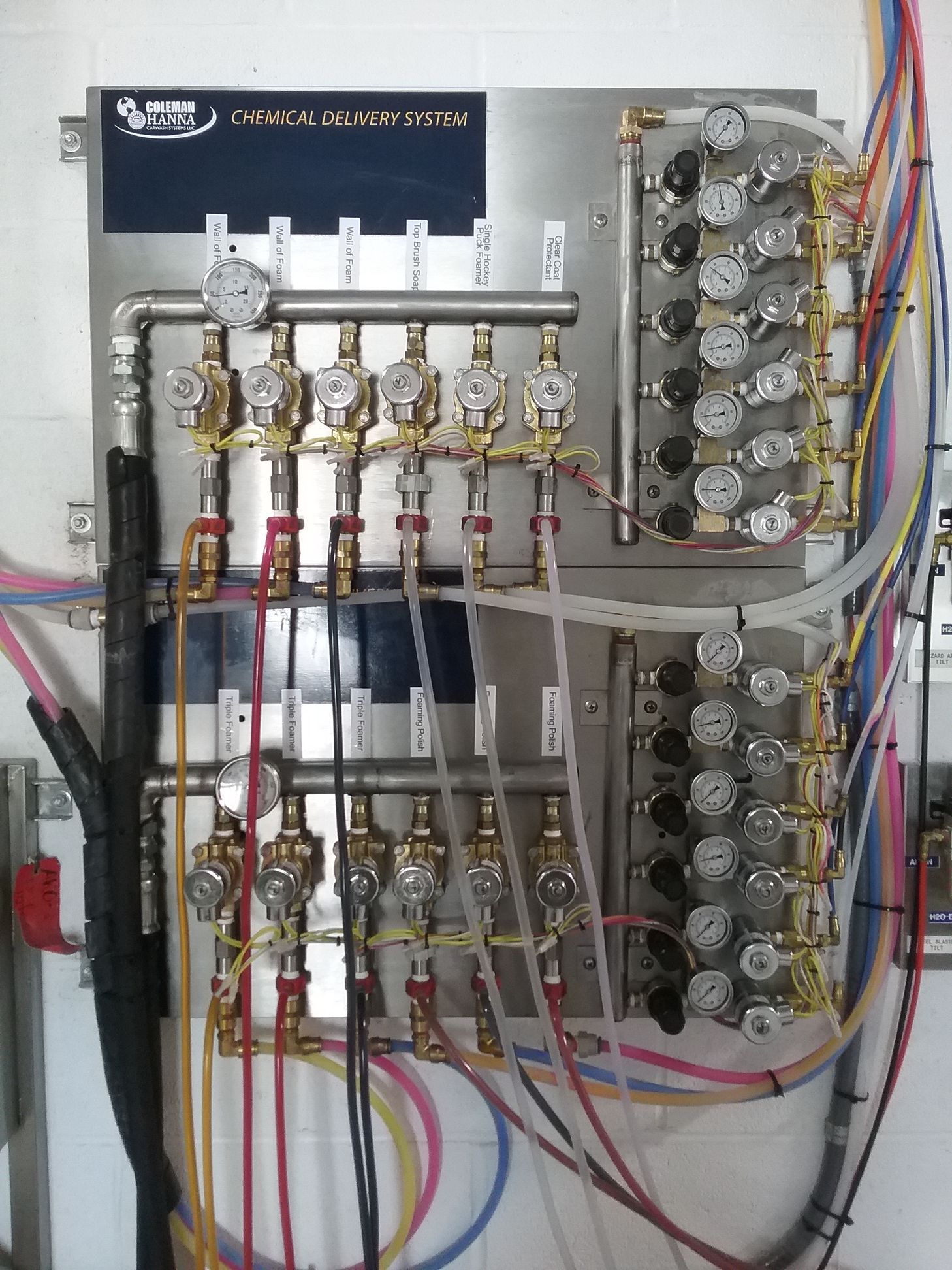 Panel with brass fittings, gauges, and colored tubes. Likely a pressure regulation system, mounted on a wall.