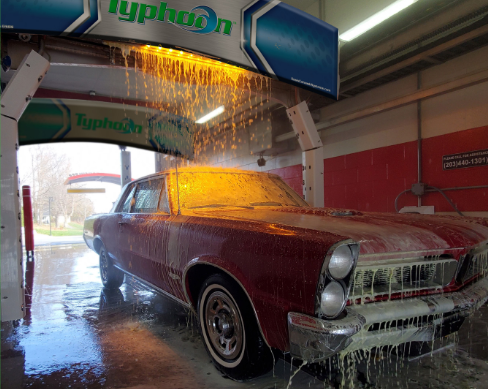 A red vintage car being washed in a Typhoon car wash bay with yellow soap dripping over its hood.
