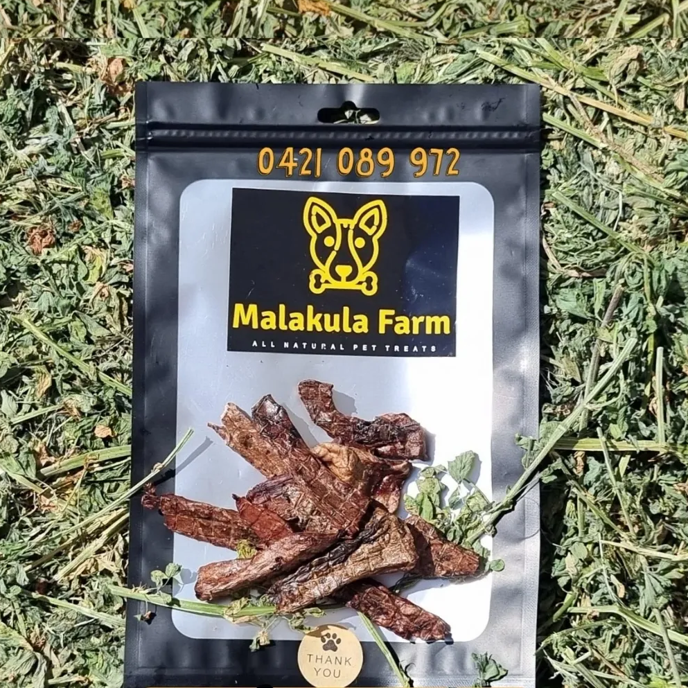 Black dog treat bag with Malakula Farm logo and dog treats on grass.