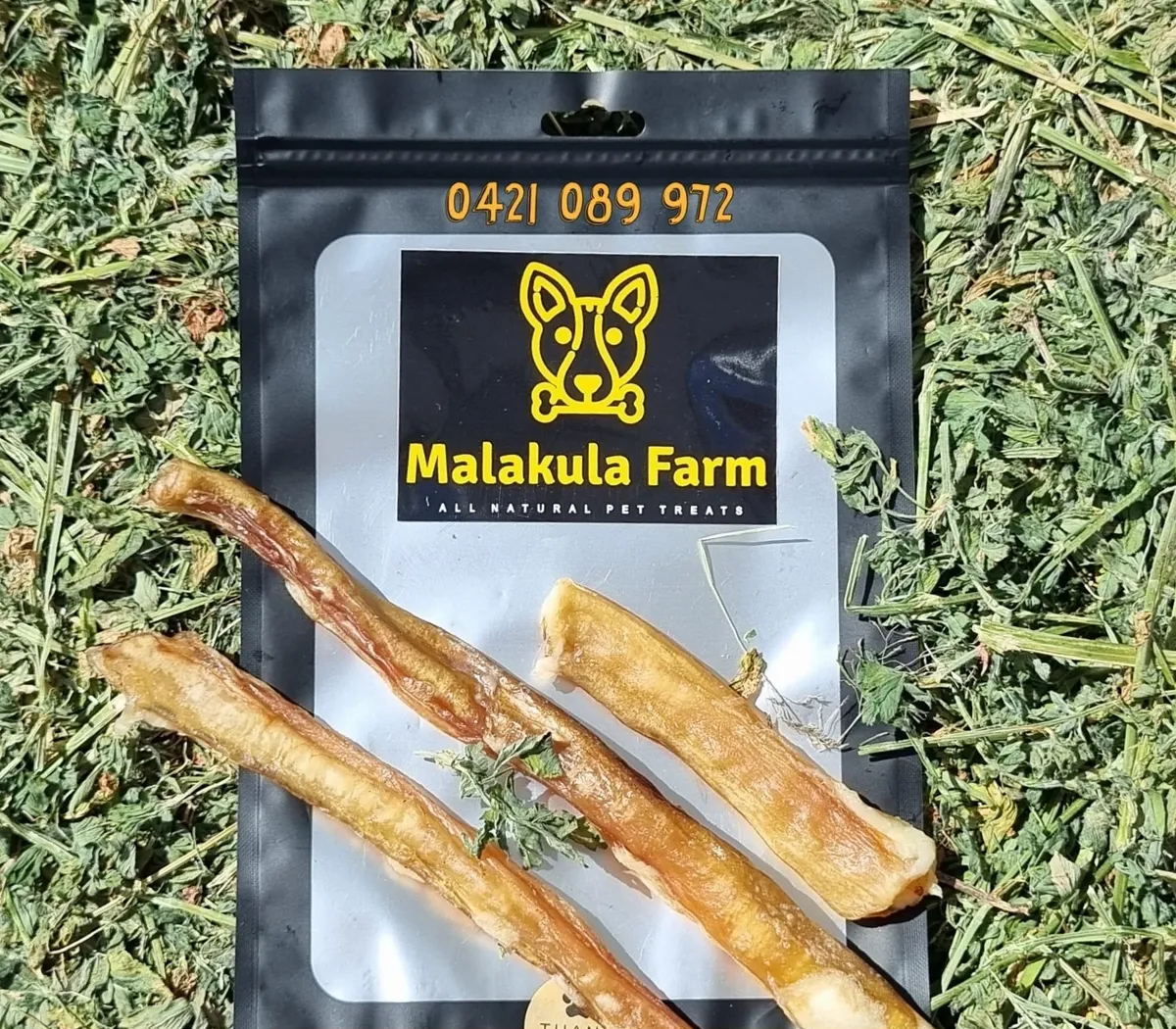 Dog treats from Malakula Farm in a black bag on a grassy surface. Treats are tan and curled.