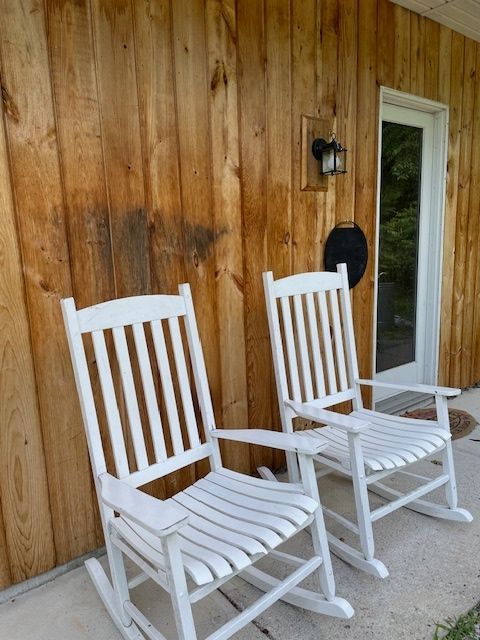 Two white rocking chairs in front of a wooden building