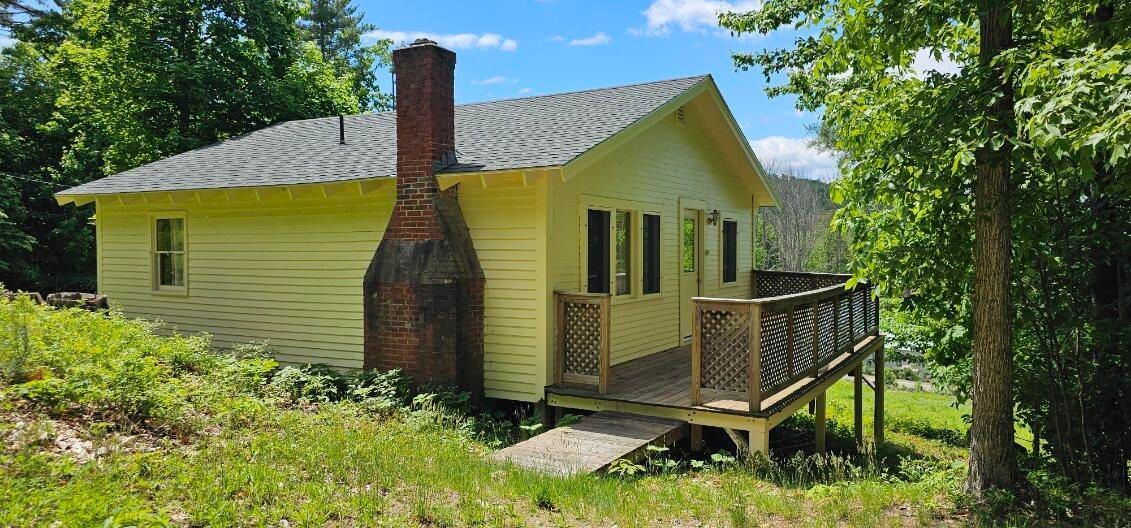 A small yellow house with a deck and a chimney in the middle of a field.