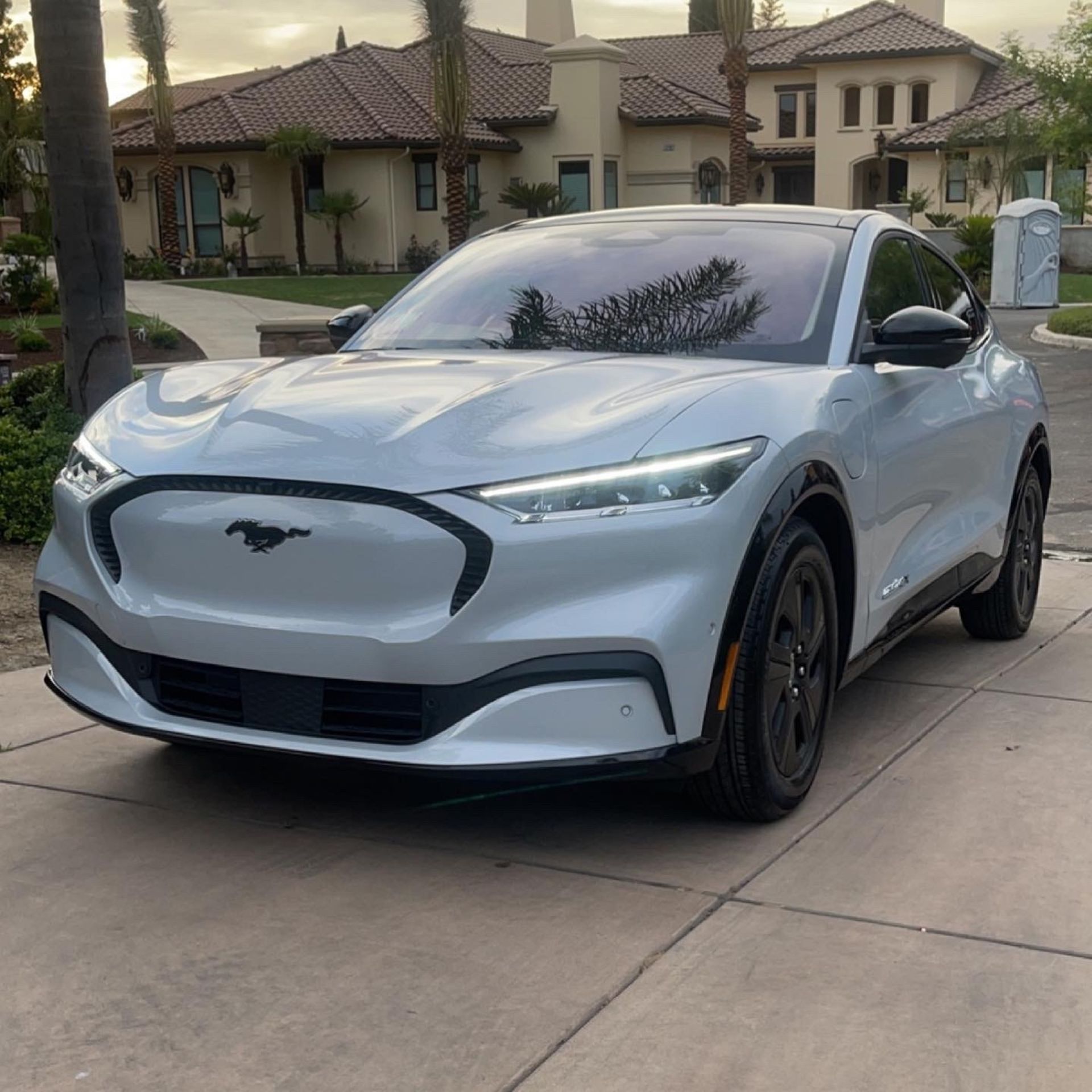 A silver mustang mach e is parked in a driveway in front of a house.