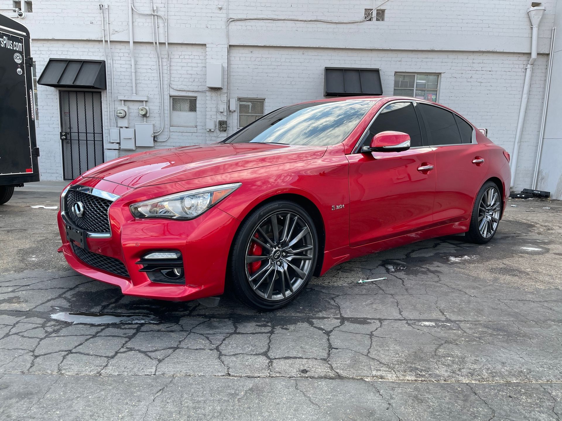 A red car is parked in a parking lot in front of a white building.