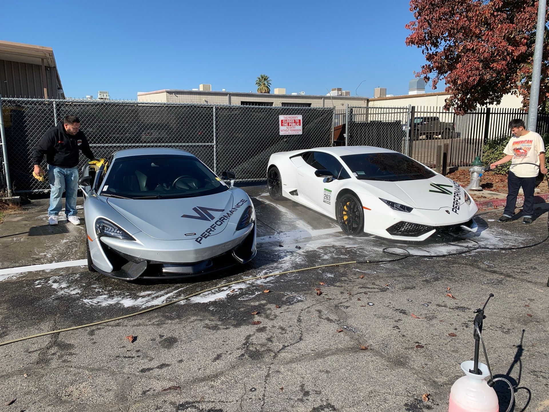 Two sports cars are being washed in a parking lot.