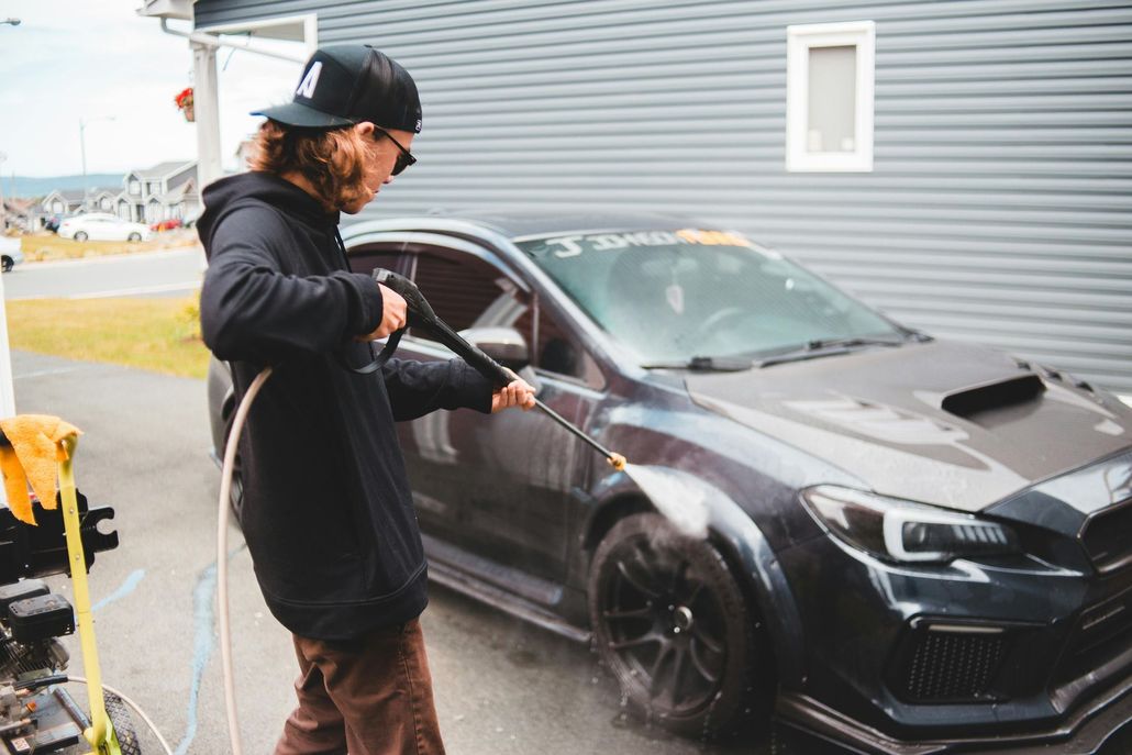 A man is washing a car with a high pressure washer.