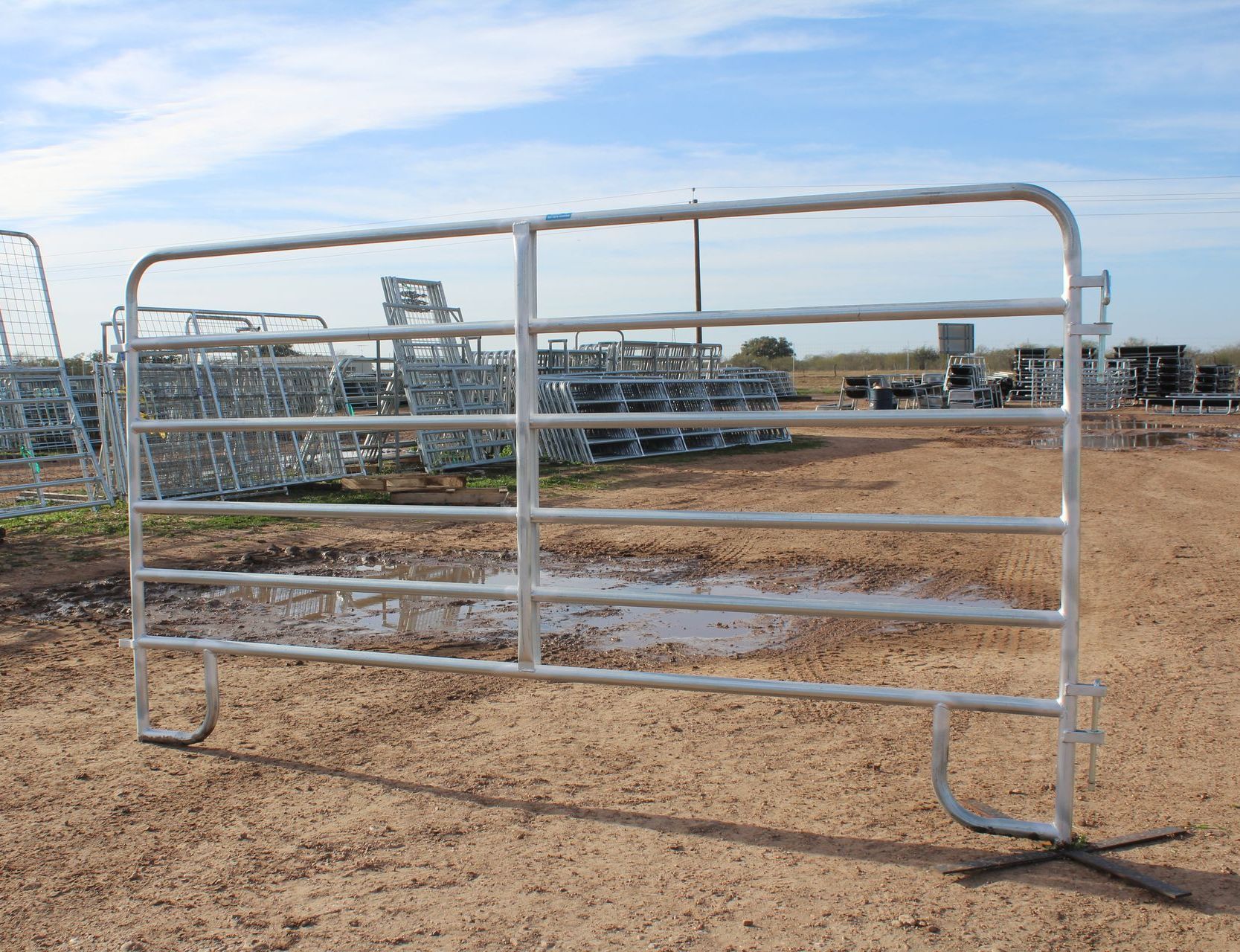 A metal gate is sitting in the middle of a dirt field.