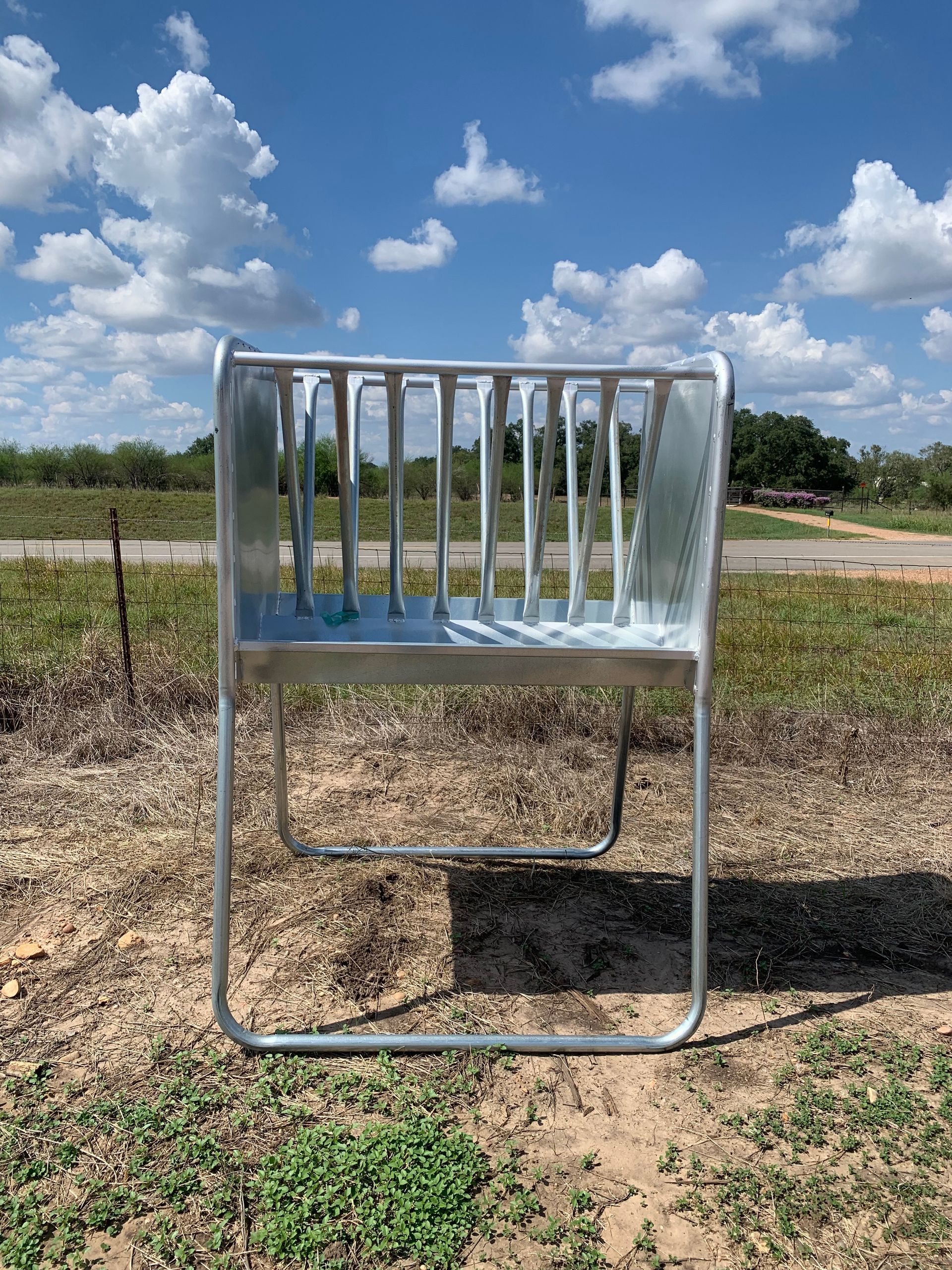 A metal hay rack is sitting in the middle of a field.