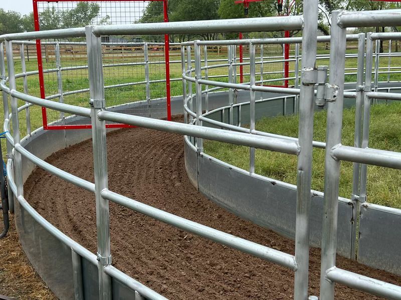 A round pen with a metal fence and a red gate