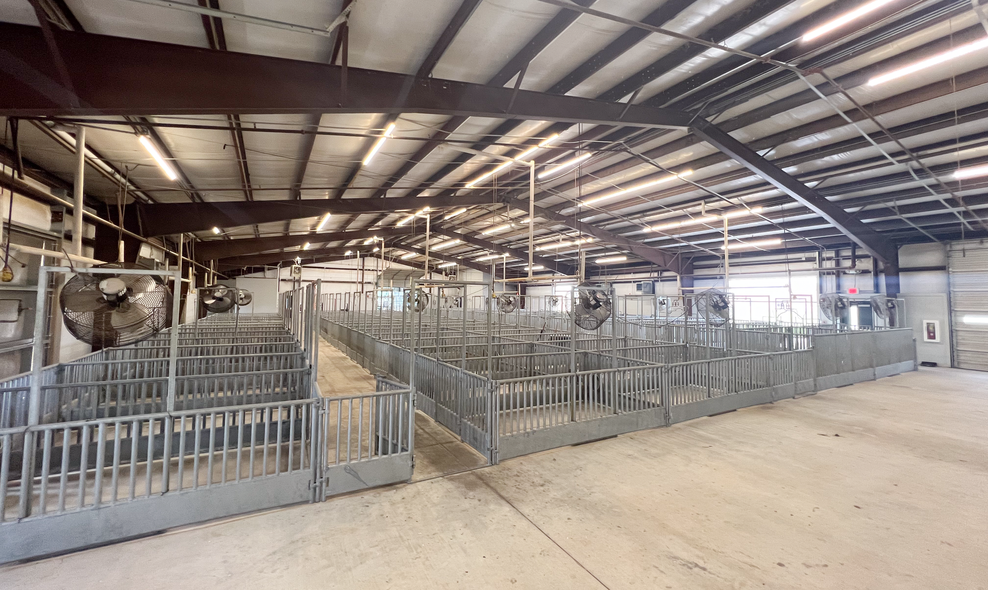 A large warehouse with a lot of fences and fans on the ceiling.