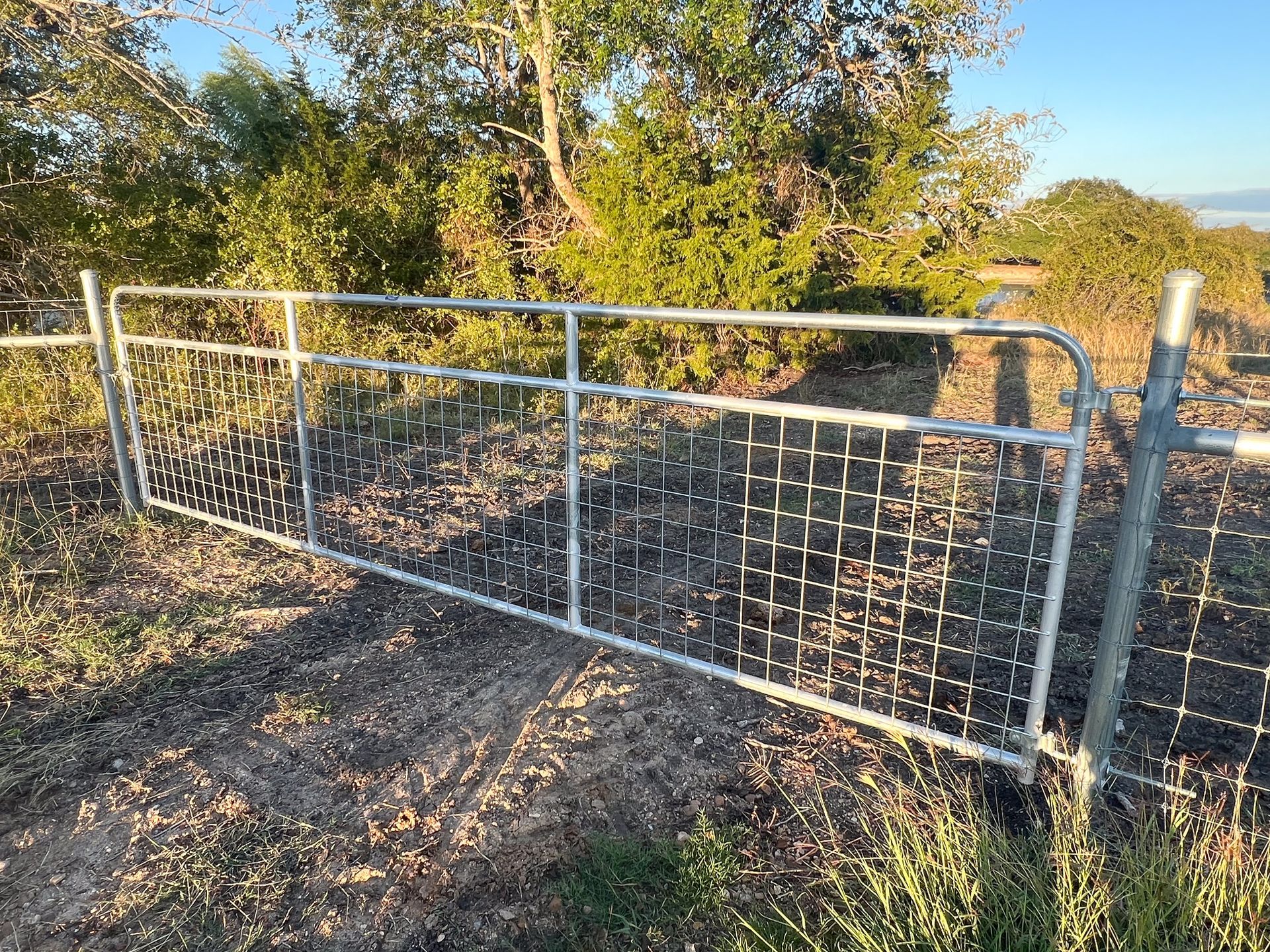 A metal gate is sitting in the middle of a field next to a barbed wire fence.