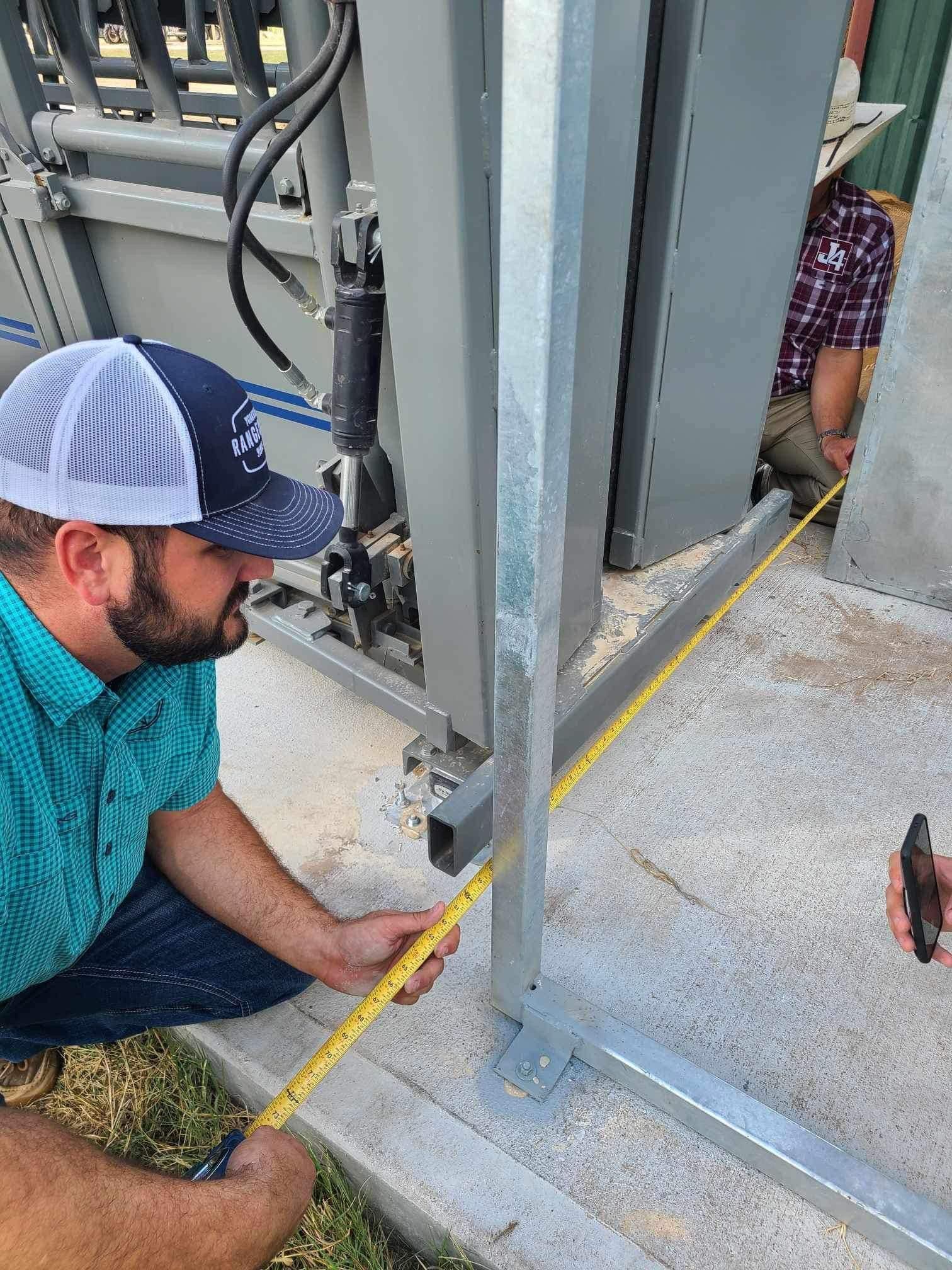 A man is measuring a deer working chute with a tape measure.