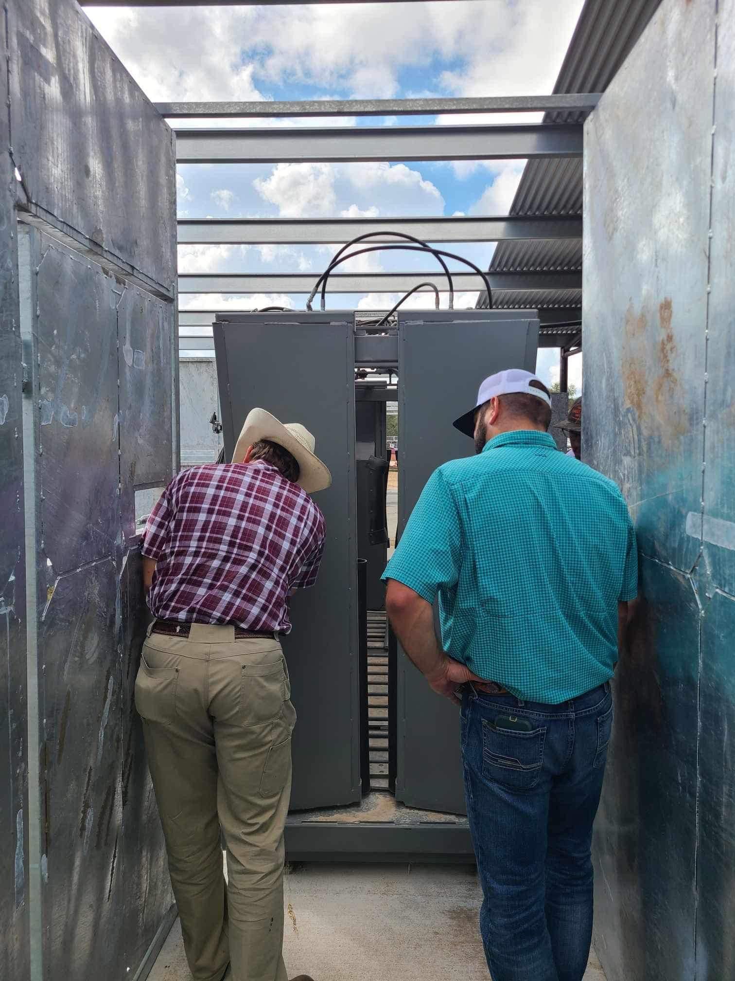 Two men are standing in a narrow hallway looking at a machine.