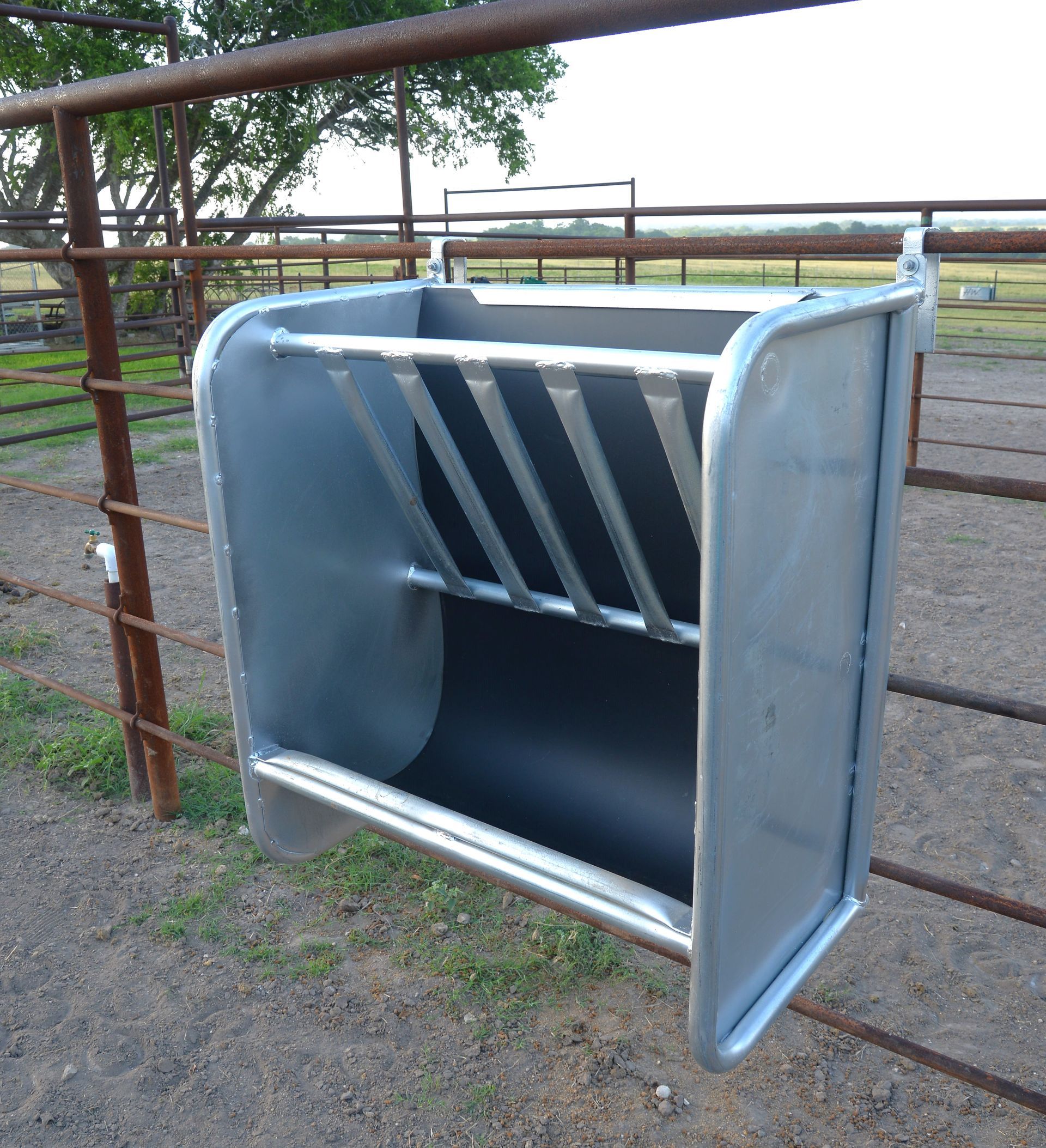 A metal feeder is hanging from a fence in a field