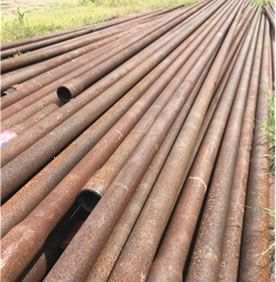 A bunch of rusty pipes are sitting on top of each other in a field.