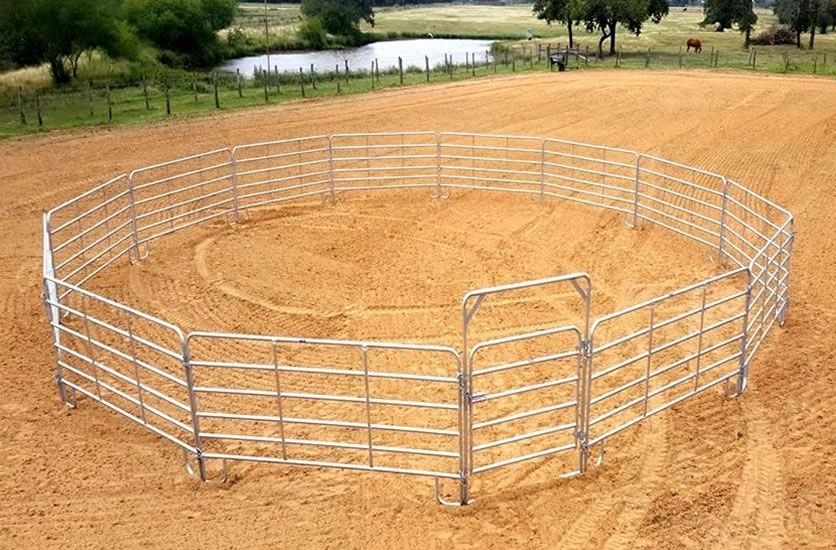 A round pen with a gate in the middle of a dirt field.