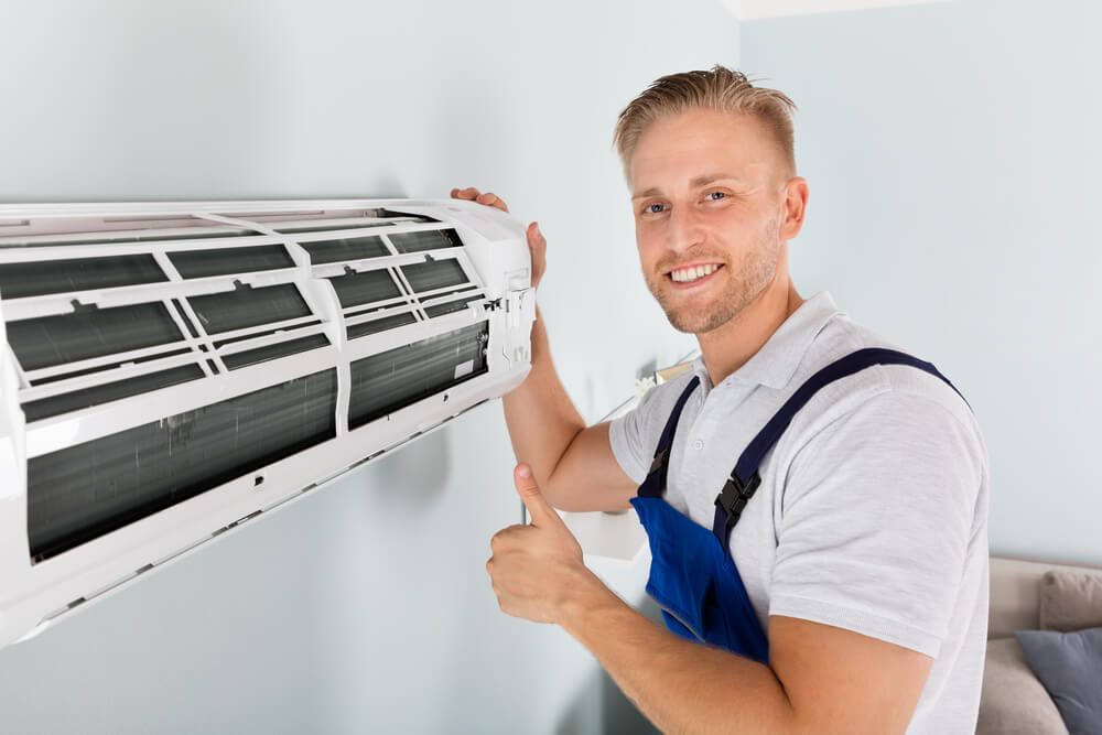 A Man Is Fixing an Air Conditioner and Giving a Thumbs Up — Care Mechanical Services in Wagga Wagga, NSW
