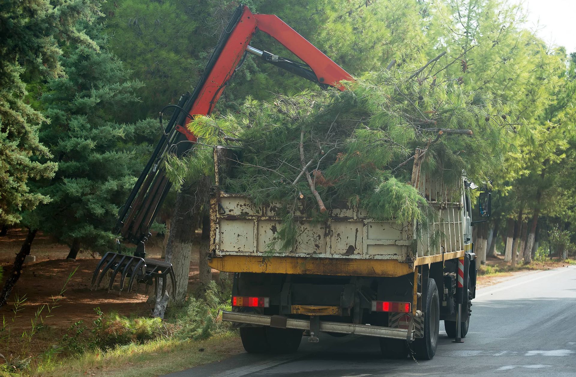 A truck with a crane on the back is driving down a road.