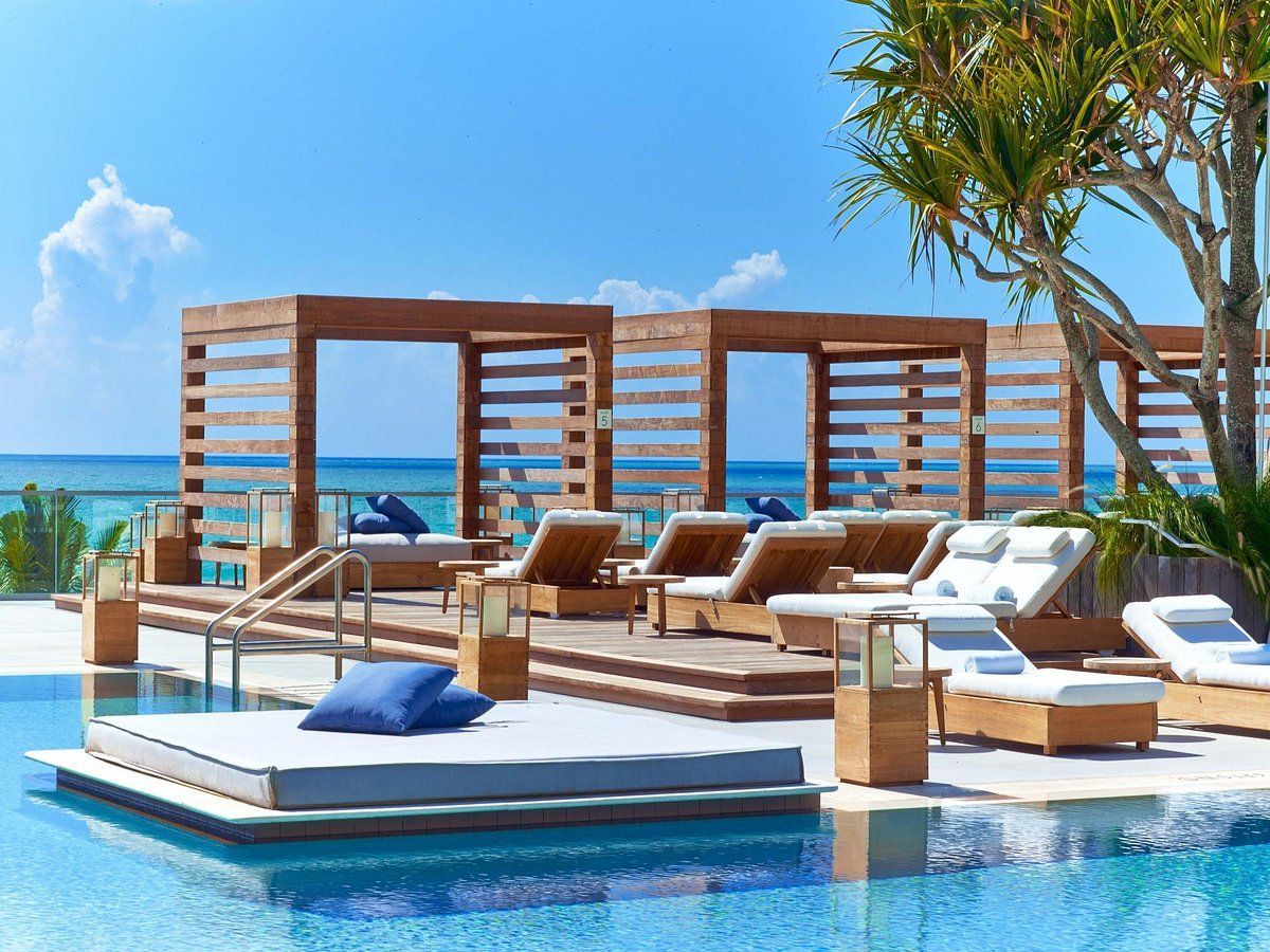 A large swimming pool surrounded by chairs and cabana 's with a view of the ocean.