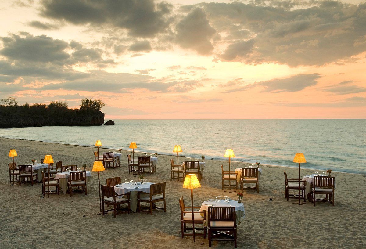 Tables and chairs are set up on the beach at sunset